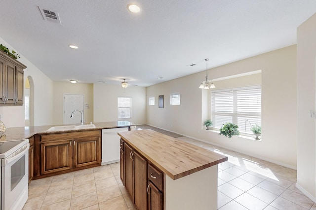 kitchen featuring light tile patterned floors, arched walkways, butcher block countertops, white appliances, and a sink