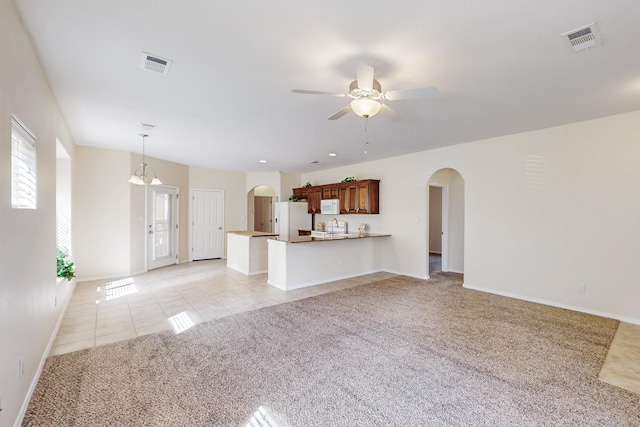 unfurnished living room featuring arched walkways, light colored carpet, visible vents, and light tile patterned floors