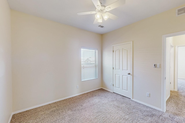 carpeted empty room with baseboards, visible vents, and a ceiling fan