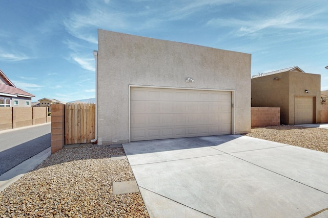 exterior space featuring a garage, concrete driveway, fence, and stucco siding