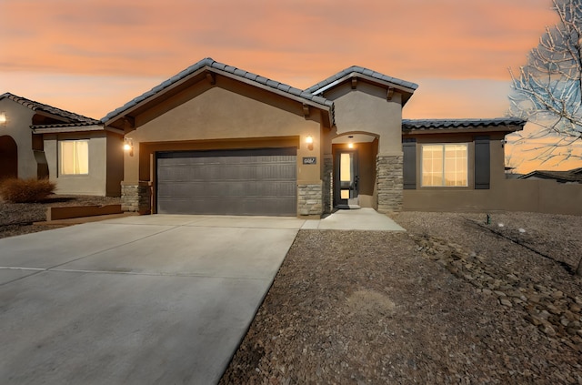 mediterranean / spanish-style home with an attached garage, stone siding, concrete driveway, and stucco siding