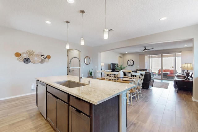 kitchen featuring light wood-style flooring, stainless steel dishwasher, open floor plan, a sink, and an island with sink