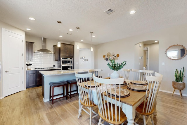 dining space featuring arched walkways, light wood-type flooring, visible vents, and recessed lighting