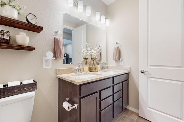 full bath with baseboards, a sink, toilet, and double vanity