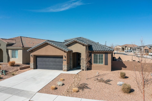 mediterranean / spanish-style home featuring a tile roof, stucco siding, an attached garage, stone siding, and driveway