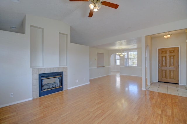 unfurnished living room featuring ceiling fan with notable chandelier, a fireplace, wood finished floors, and baseboards