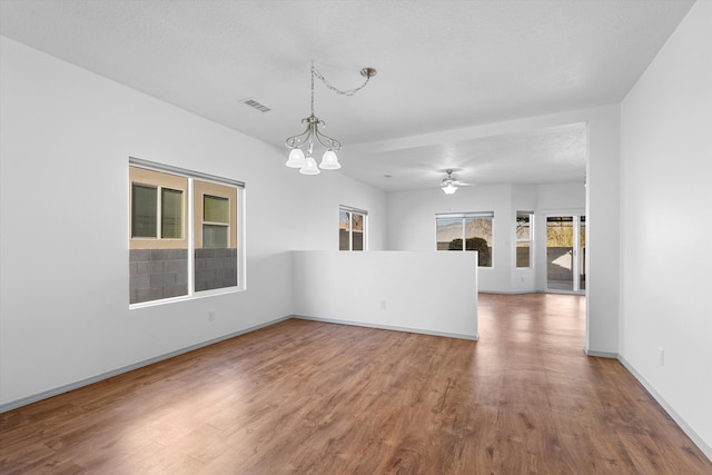 unfurnished room with ceiling fan with notable chandelier, wood finished floors, visible vents, and baseboards