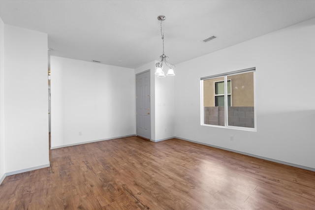 spare room with an inviting chandelier, visible vents, baseboards, and wood finished floors