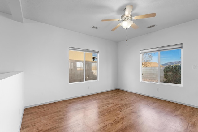 empty room with a ceiling fan, wood finished floors, visible vents, and baseboards