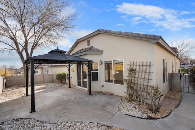 rear view of property featuring fence private yard, stucco siding, a patio, and a gazebo