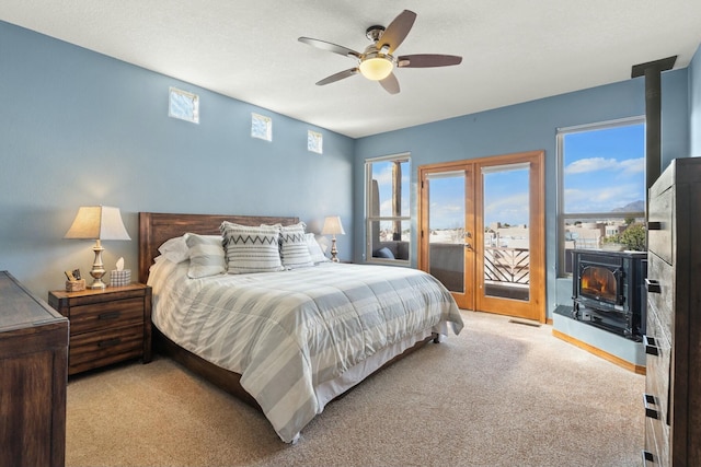 bedroom with light colored carpet, visible vents, a ceiling fan, a wood stove, and access to outside