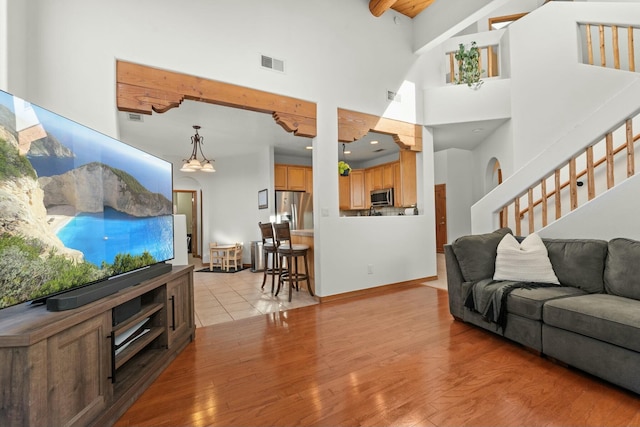 living room featuring stairway, light wood-type flooring, a towering ceiling, and visible vents