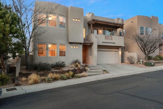 pueblo-style home with an attached garage, concrete driveway, and stucco siding