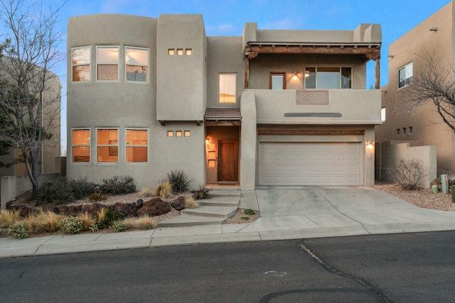 adobe home featuring concrete driveway, a balcony, an attached garage, and stucco siding