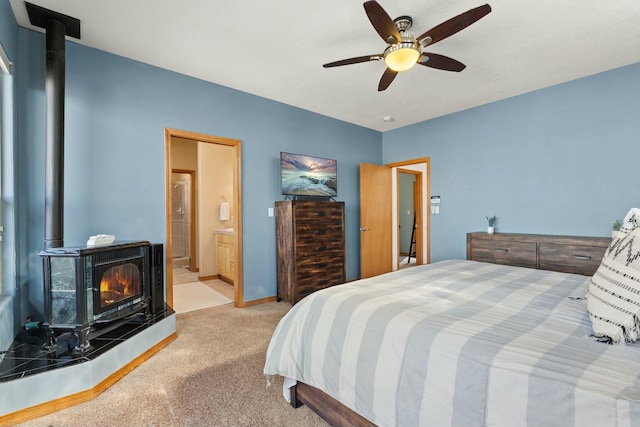 carpeted bedroom with a ceiling fan, connected bathroom, a wood stove, and baseboards