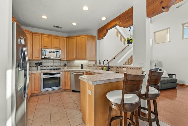 kitchen featuring tile countertops, a breakfast bar area, a peninsula, stainless steel appliances, and a sink