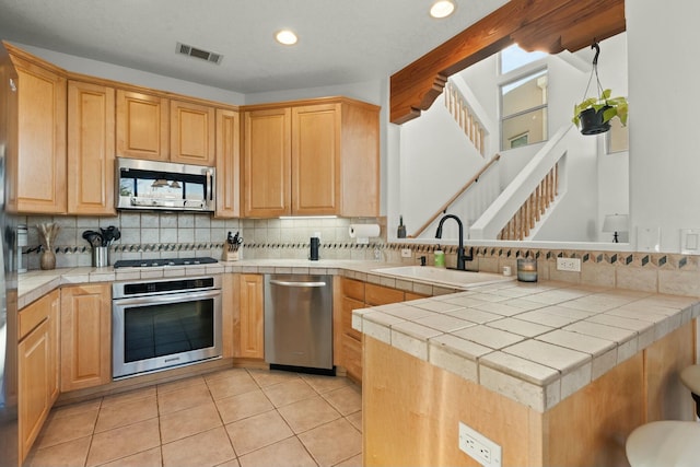 kitchen with tile countertops, stainless steel appliances, a peninsula, a sink, and visible vents