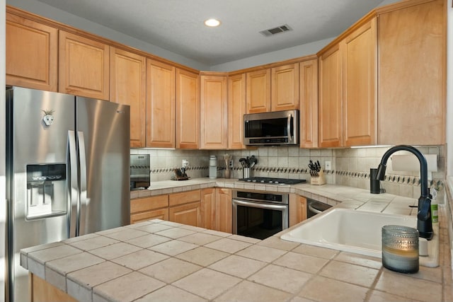 kitchen with tile countertops, a sink, visible vents, appliances with stainless steel finishes, and tasteful backsplash