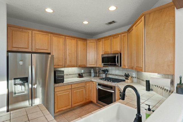 kitchen featuring light tile patterned floors, tasteful backsplash, tile counters, stainless steel appliances, and recessed lighting