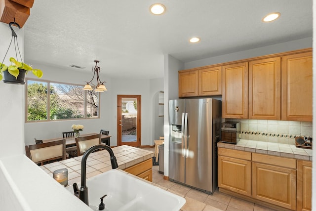 kitchen with arched walkways, stainless steel fridge with ice dispenser, tile countertops, a sink, and backsplash