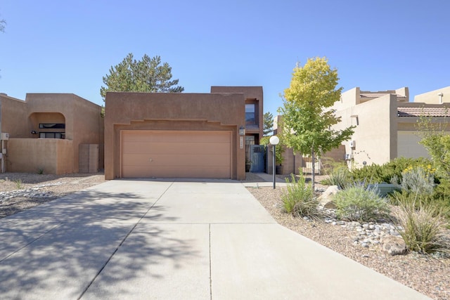 pueblo-style home with concrete driveway, an attached garage, and stucco siding