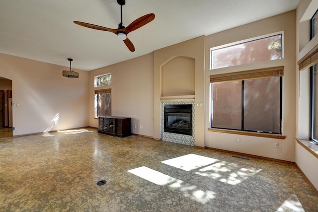 unfurnished living room featuring ceiling fan, a tile fireplace, visible vents, and baseboards