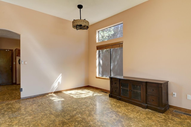 unfurnished room featuring baseboards, visible vents, and arched walkways