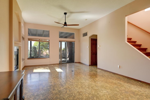 spare room featuring visible vents, baseboards, a glass covered fireplace, ceiling fan, and stairway