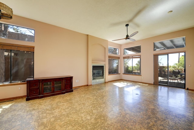 unfurnished living room featuring a tiled fireplace, a towering ceiling, a ceiling fan, and baseboards