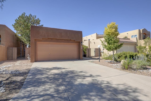 pueblo revival-style home with a garage, a gate, fence, and stucco siding