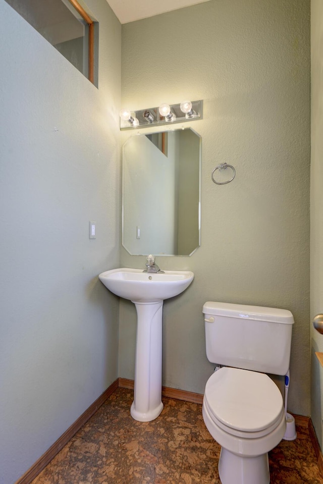 bathroom with toilet, stone finish flooring, and baseboards