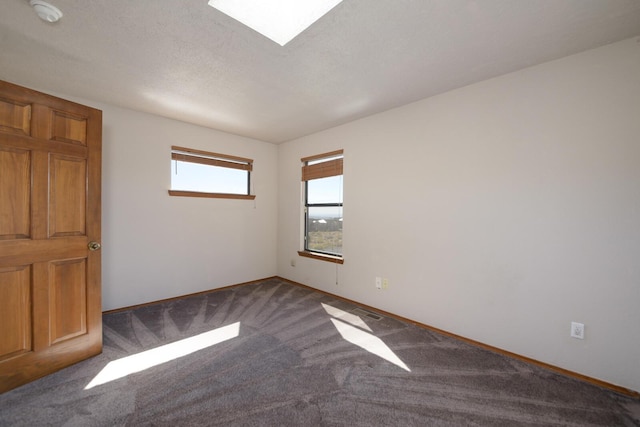 carpeted spare room featuring a skylight, a textured ceiling, and baseboards