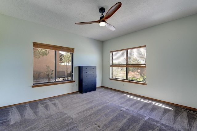 empty room featuring a textured ceiling, carpet floors, visible vents, and a healthy amount of sunlight