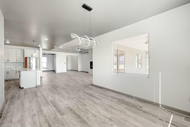 unfurnished living room featuring a ceiling fan, a fireplace, light wood-style floors, and baseboards