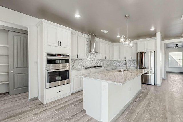 kitchen with wood finish floors, stainless steel appliances, white cabinetry, a sink, and wall chimney exhaust hood