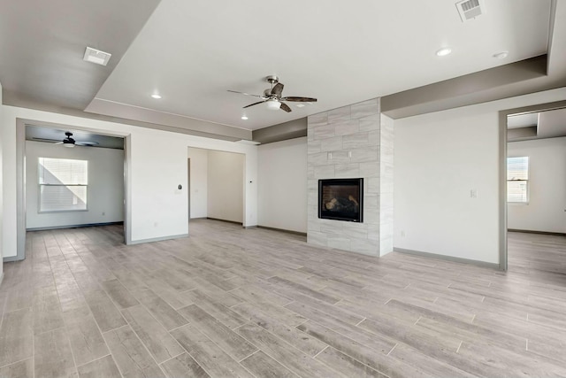 unfurnished living room featuring light wood-style floors, ceiling fan, visible vents, and a tiled fireplace