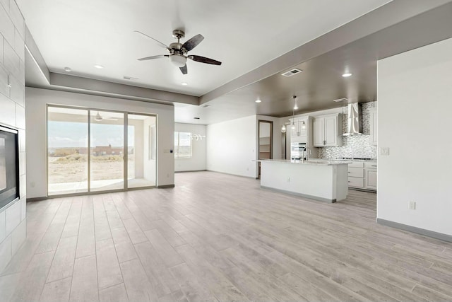 unfurnished living room featuring baseboards, visible vents, light wood finished floors, and ceiling fan with notable chandelier