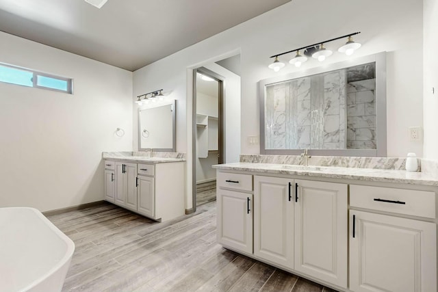 full bath with wood finished floors, two vanities, a sink, baseboards, and a tile shower