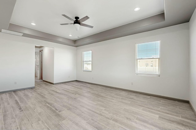 unfurnished room featuring a raised ceiling, light wood-style flooring, and baseboards