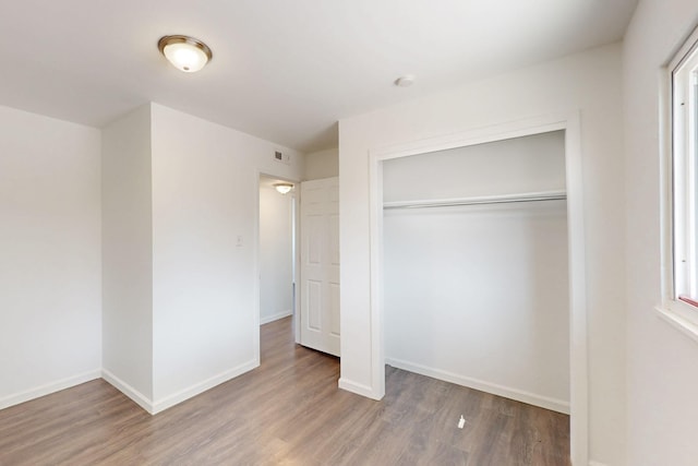 unfurnished bedroom featuring a closet, wood finished floors, visible vents, and baseboards