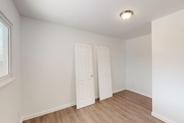 unfurnished bedroom with multiple windows, light wood-style flooring, and baseboards