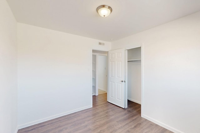 unfurnished bedroom with baseboards, a closet, visible vents, and wood finished floors