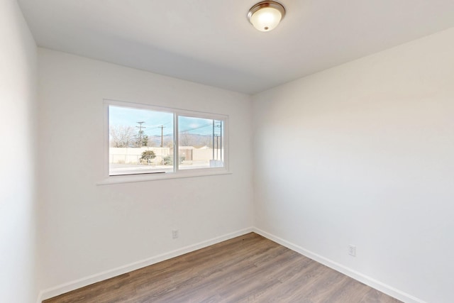 spare room with baseboards and wood finished floors