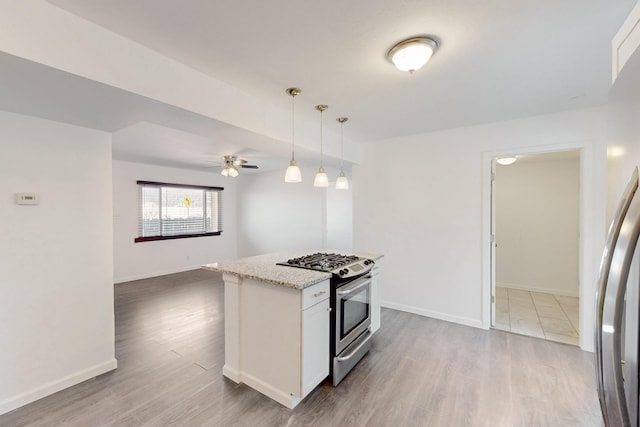 kitchen featuring stainless steel gas range oven, light stone counters, wood finished floors, white cabinetry, and baseboards