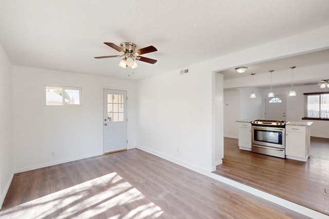 unfurnished living room with light wood-type flooring, ceiling fan, visible vents, and baseboards