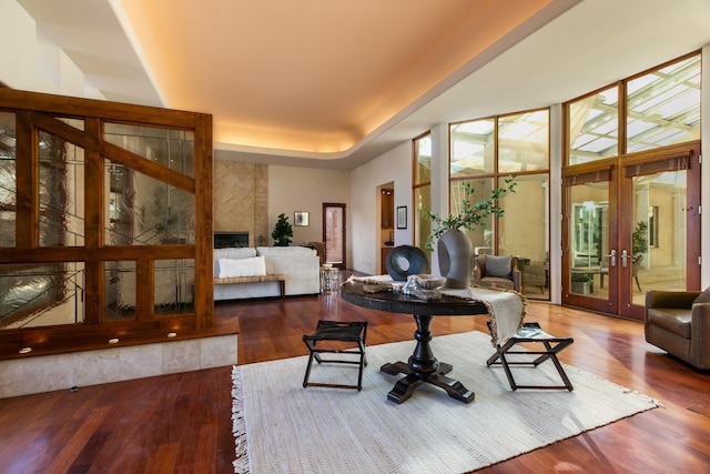 interior space featuring a raised ceiling, french doors, a tiled fireplace, and wood finished floors