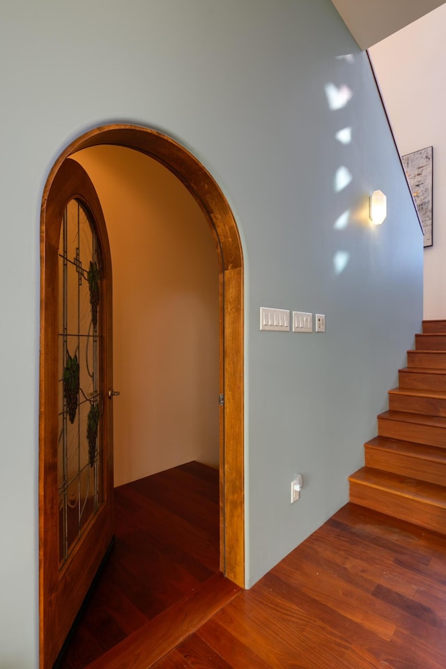 corridor featuring arched walkways, wood finished floors, and stairs