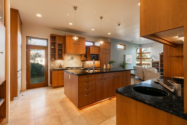 kitchen featuring black microwave, a kitchen island with sink, a sink, brown cabinets, and decorative backsplash