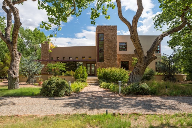 adobe home featuring stone siding, french doors, and stucco siding