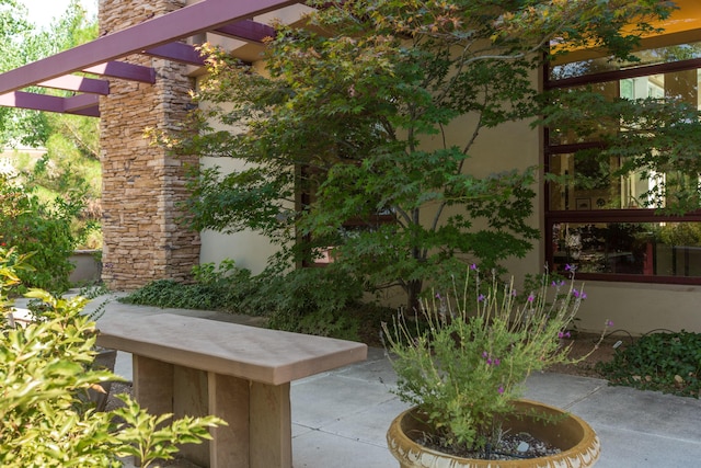 view of side of home with stone siding, a patio area, a pergola, and stucco siding